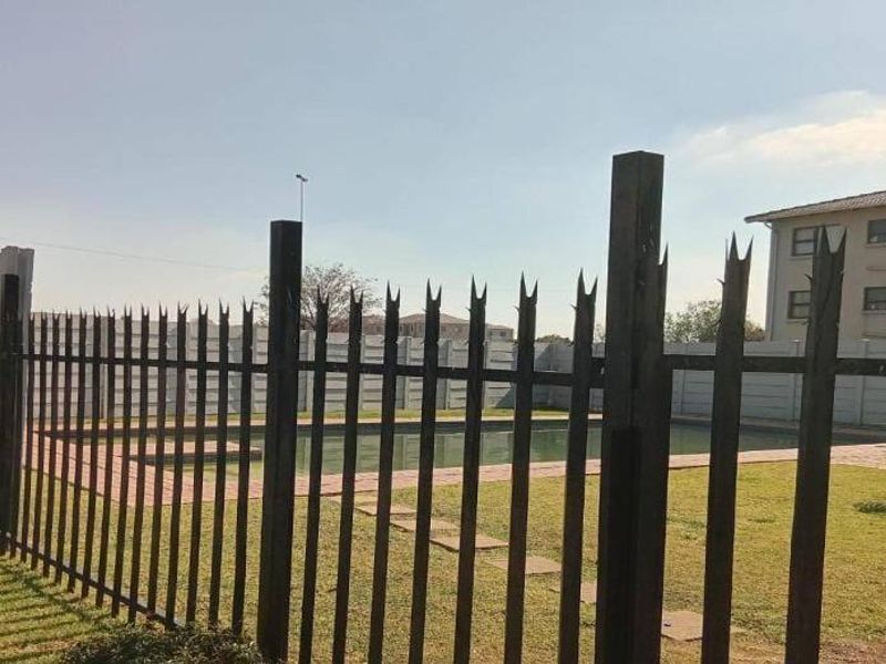 Communal swimming pool area featuring a paved surround, enclosed by a precast concrete wall and steel security fencing.