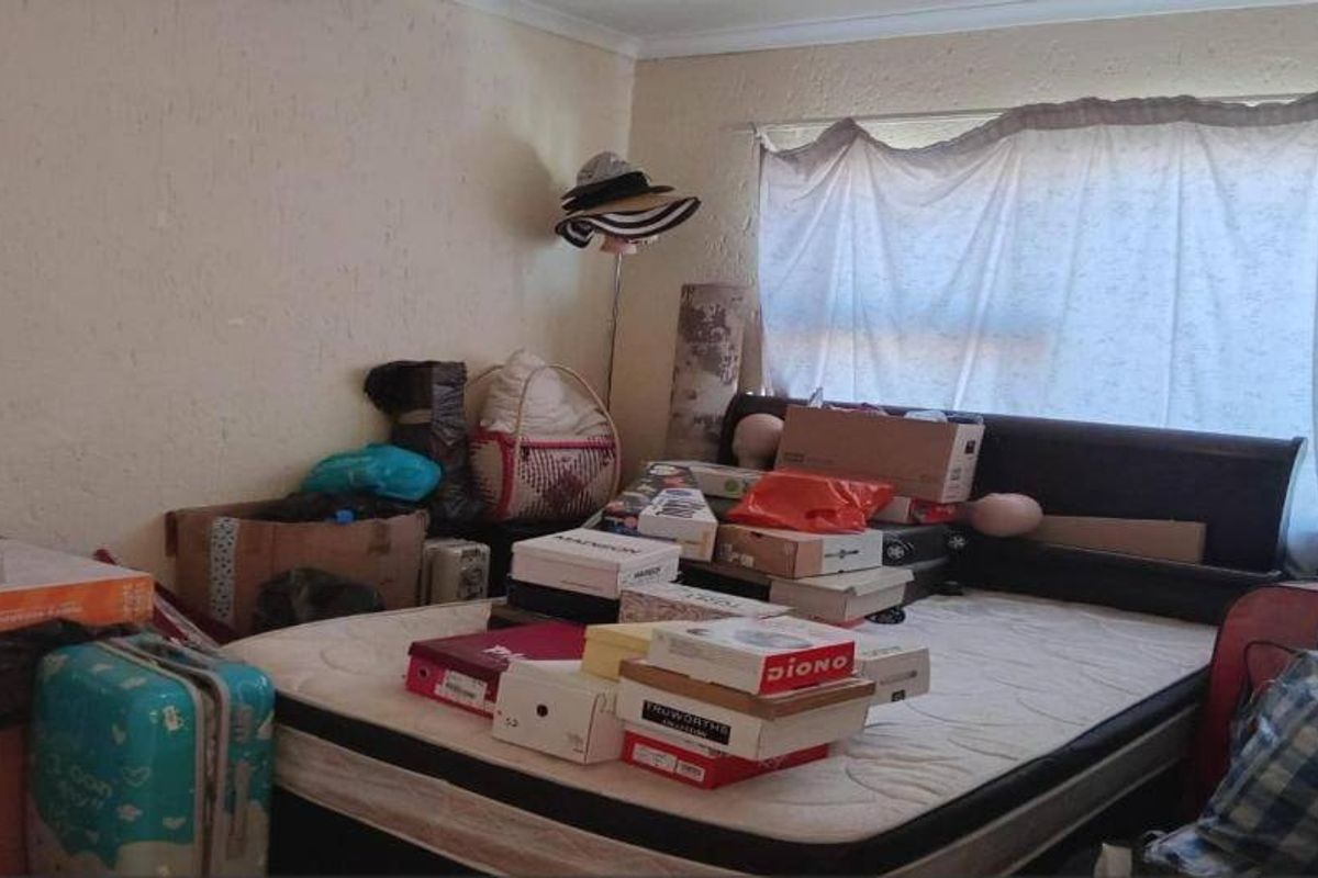 A bedroom featuring a built-in headboard, currently cluttered with personal items. The room requires cosmetic updates including wall repairs and fresh paint.