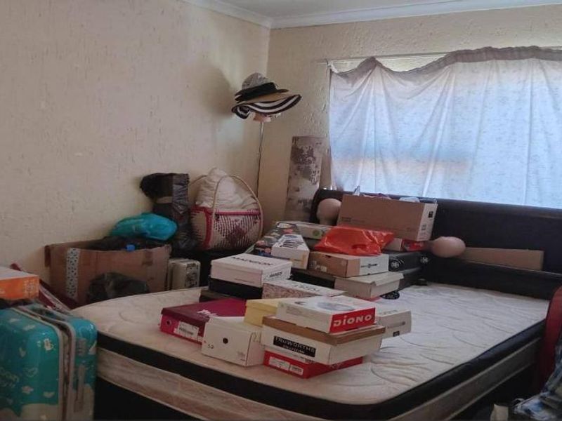 A bedroom featuring a built-in headboard, currently cluttered with personal items. The room requires cosmetic updates including wall repairs and fresh paint.