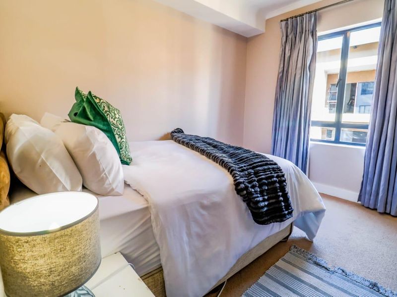 A well-maintained bedroom featuring neutral wall tones, carpeted flooring, and a large window with curtain tracks, providing natural light.