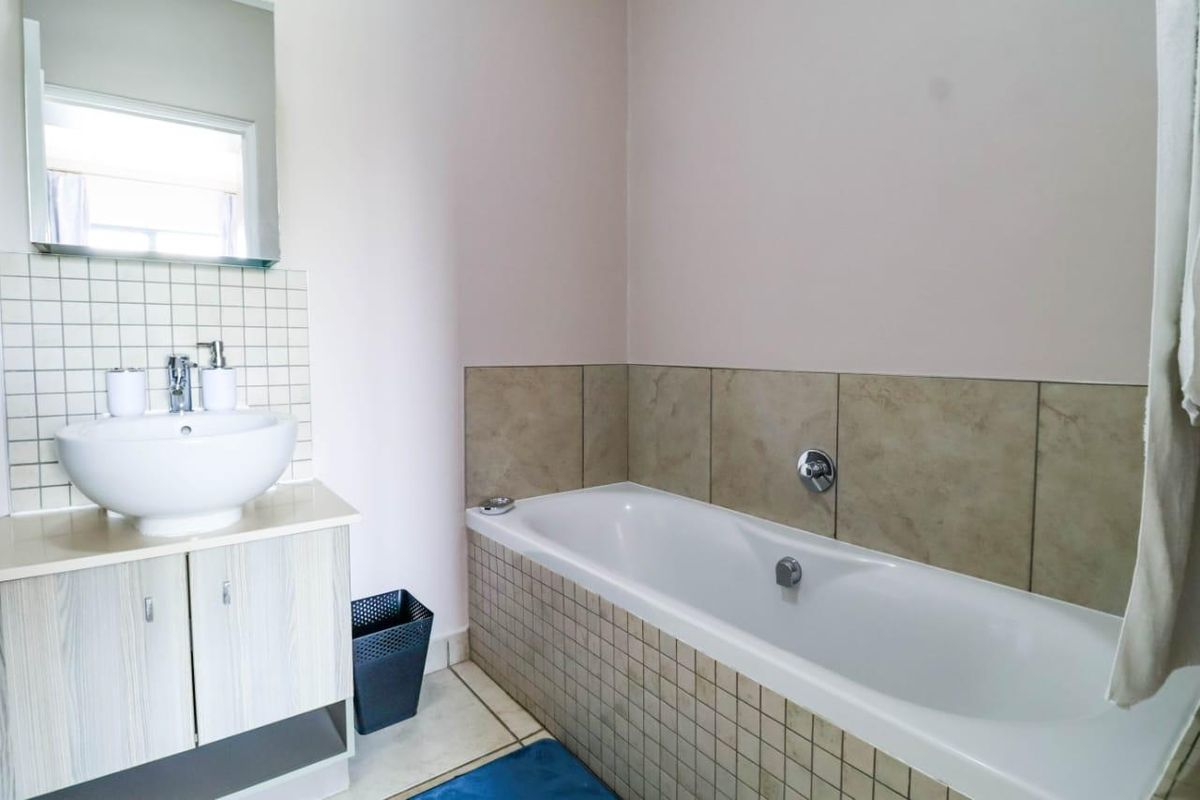 A functional bathroom featuring a vessel sink vanity, wall mirror, and a tiled bathtub surround with neutral wall finishes.
