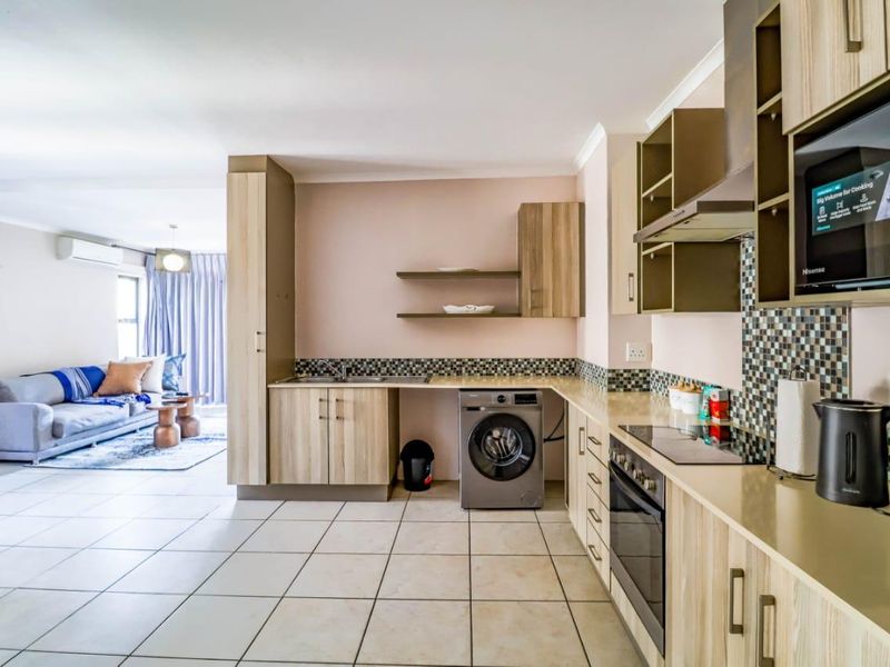 Modern open-plan kitchen featuring light wood cabinetry, mosaic backsplash, and integrated appliances, flowing seamlessly into a comfortable living area with air conditioning.