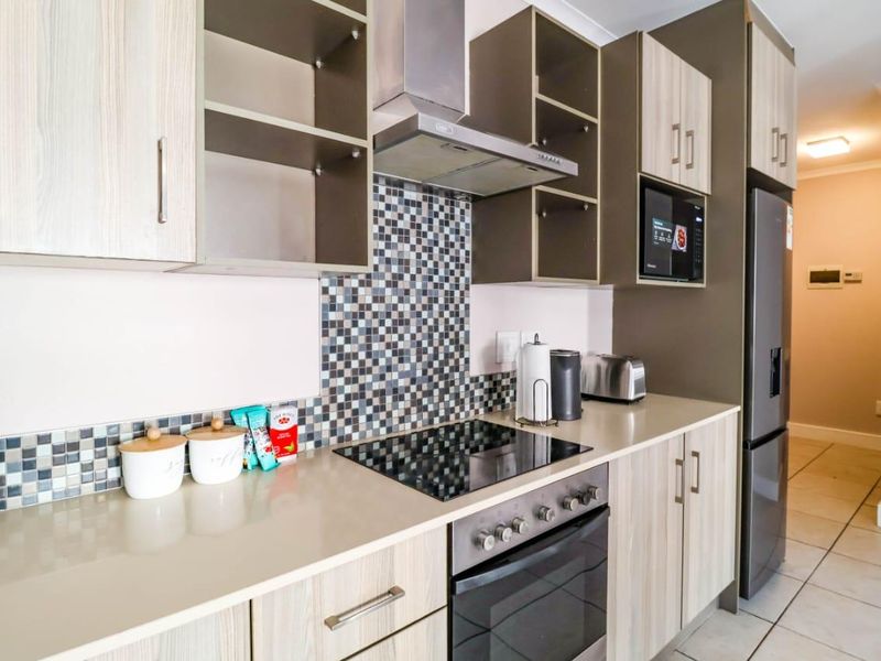 Modern kitchen featuring light wood-tone cabinetry, stone countertops, mosaic tile backsplash, and integrated stainless steel appliances including an oven and hob.