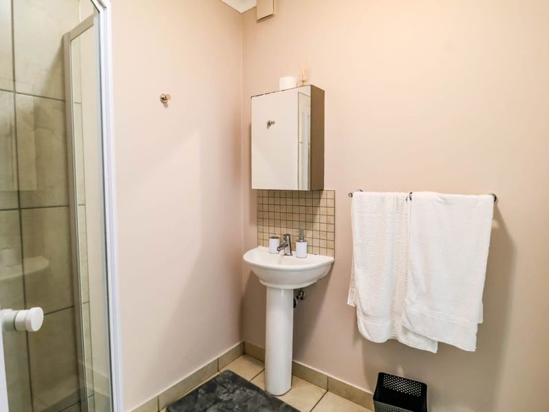 A functional bathroom featuring a pedestal basin with tiled splashback, a shower enclosure, and a wall-mounted medicine cabinet.