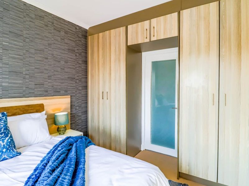 A well-maintained bedroom featuring extensive built-in wooden cabinetry and a modern frosted glass door, complemented by textured feature wallpaper.