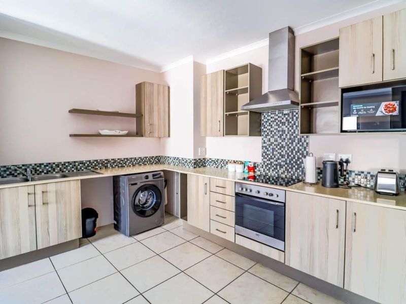 A functional kitchen featuring light wood-finish cabinetry, mosaic tile backsplash, integrated stainless steel appliances, and ceramic floor tiling.