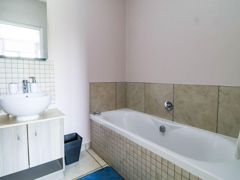 A functional bathroom featuring a vessel sink vanity, wall mirror, and a tiled bathtub surround with neutral wall finishes.