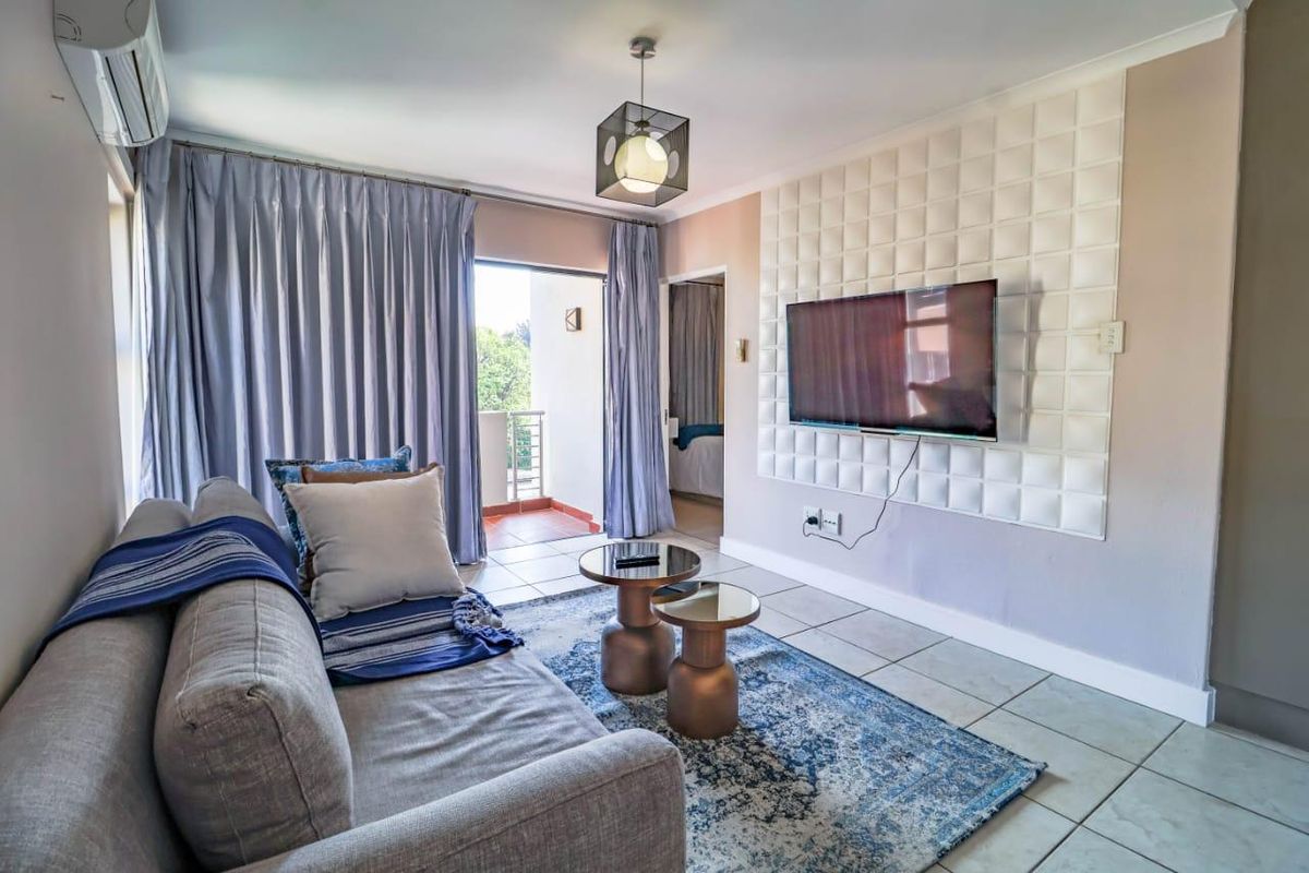 A well-lit living room featuring tiled flooring, a decorative textured feature wall, and direct access to an outdoor balcony through sliding glass doors.