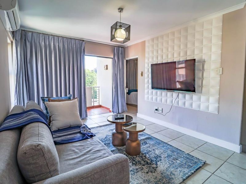 A well-lit living room featuring tiled flooring, a decorative textured feature wall, and direct access to an outdoor balcony through sliding glass doors.