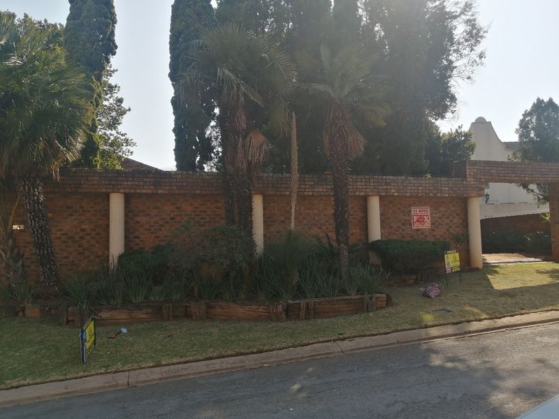 Front view of the property featuring a brick boundary wall with integrated concrete columns and established garden landscaping.