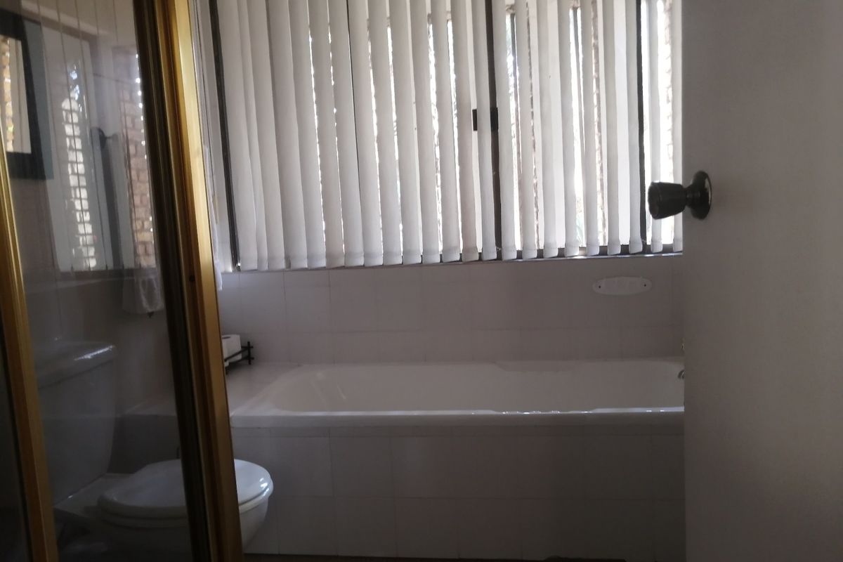 A functional bathroom featuring a built-in bathtub, toilet, and vertical blinds, offering a clean and simple layout ready for potential cosmetic updates.