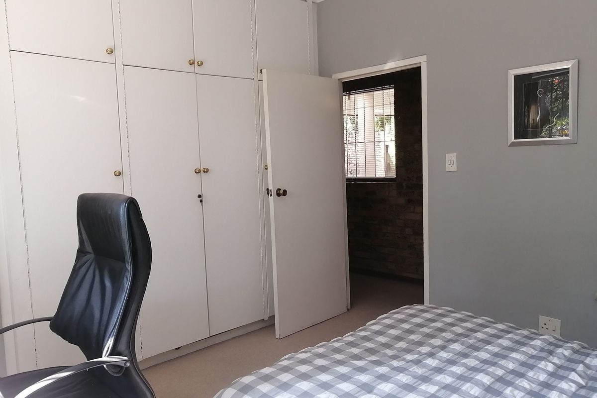 A bedroom featuring extensive floor-to-ceiling built-in cupboards, neutral grey walls, and carpeted flooring, providing ample storage space.