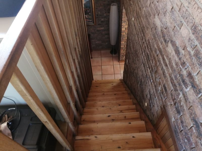 A staircase featuring wooden steps and a matching balustrade, complemented by an exposed brick wall and tiled flooring at the landing.