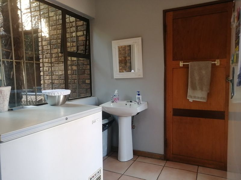 A functional laundry area featuring a pedestal basin, tiled flooring, and a solid timber door with access to natural light through a large window.