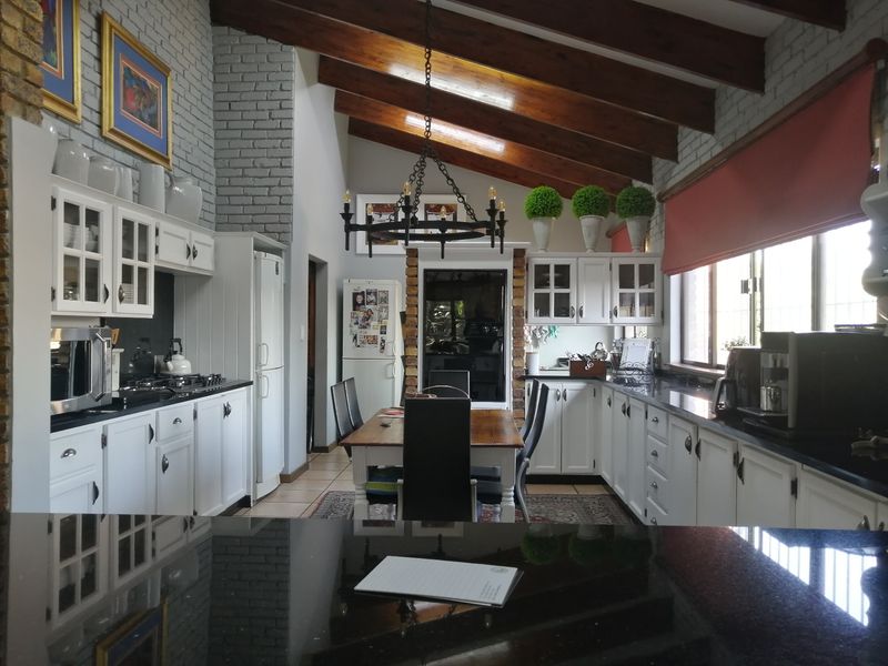 Spacious open-plan kitchen and dining area featuring high vaulted ceilings with exposed timber beams, brick accents, and modern white cabinetry with granite countertops.