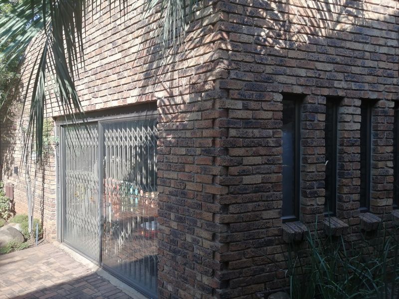 A rear exterior view of the house featuring a face brick facade, paved patio area, and a sliding glass door with a security gate.