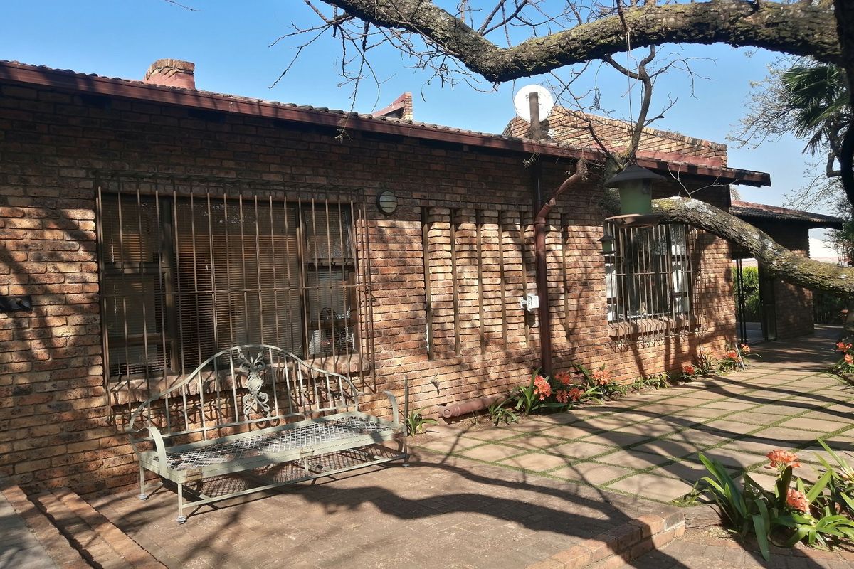 A rear exterior view of a face brick house featuring a paved patio area, security bars on windows, and established garden surroundings.