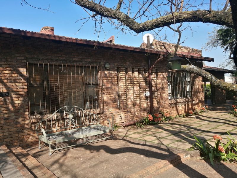 A rear exterior view of a face brick house featuring a paved patio area, security bars on windows, and established garden surroundings.