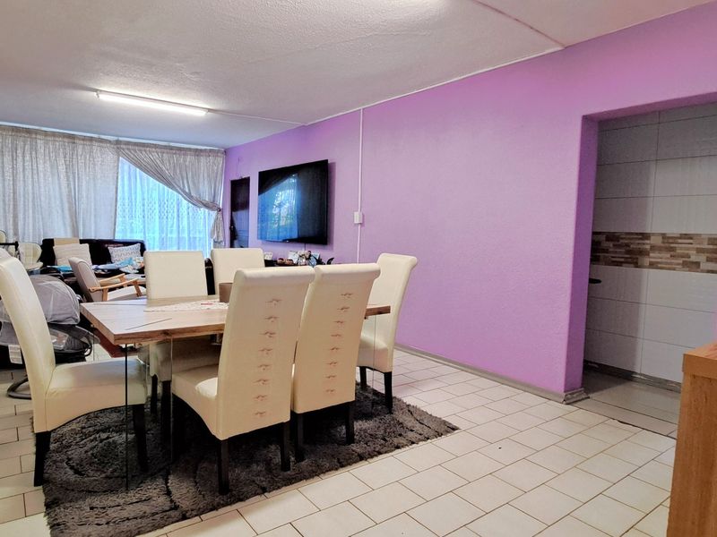 Open-plan living and dining area featuring tiled flooring and a wall-mounted television, providing a functional space for daily living.