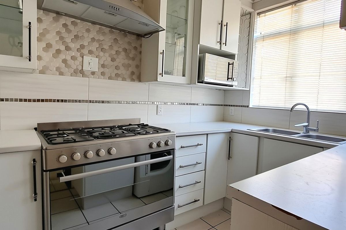 Modern kitchen featuring white cabinetry, a gas stove with extractor fan, tiled backsplash, and a double sink with ample counter space.