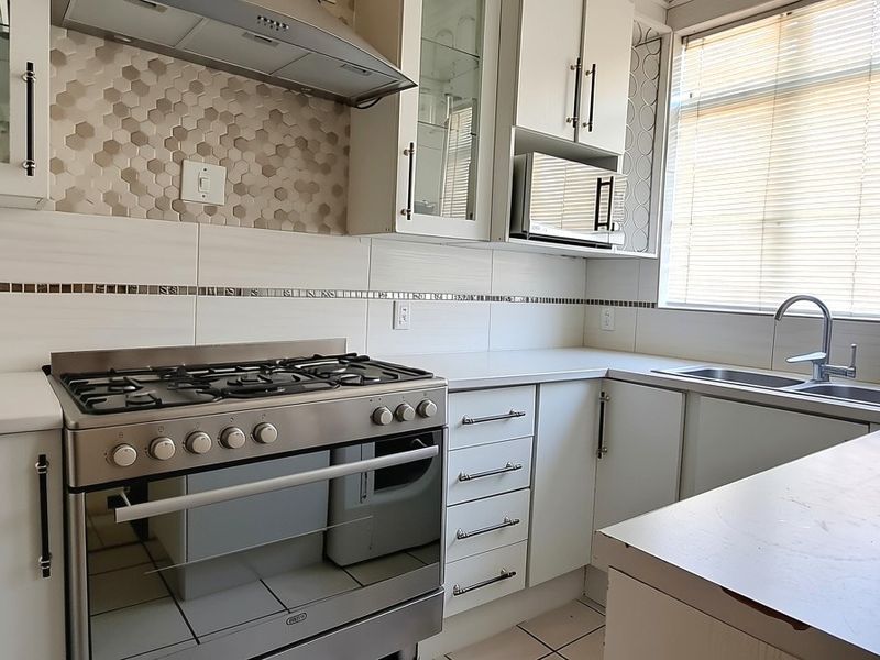 Modern kitchen featuring white cabinetry, a gas stove with extractor fan, tiled backsplash, and a double sink with ample counter space.