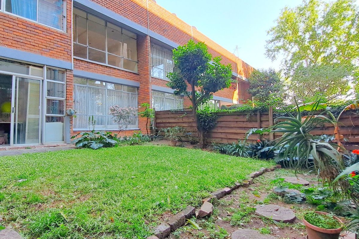 A private rear garden area featuring a lawn, paved stepping stones, and a wooden boundary fence, accessible via large sliding glass doors.