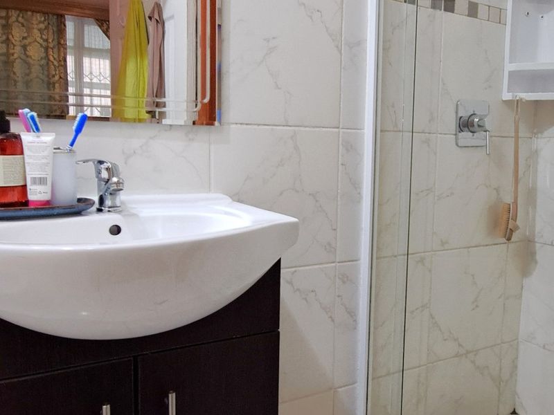 A functional bathroom featuring a dark vanity cabinet, ceramic basin, wall mirror, and a glass-enclosed shower with tiled finishes.