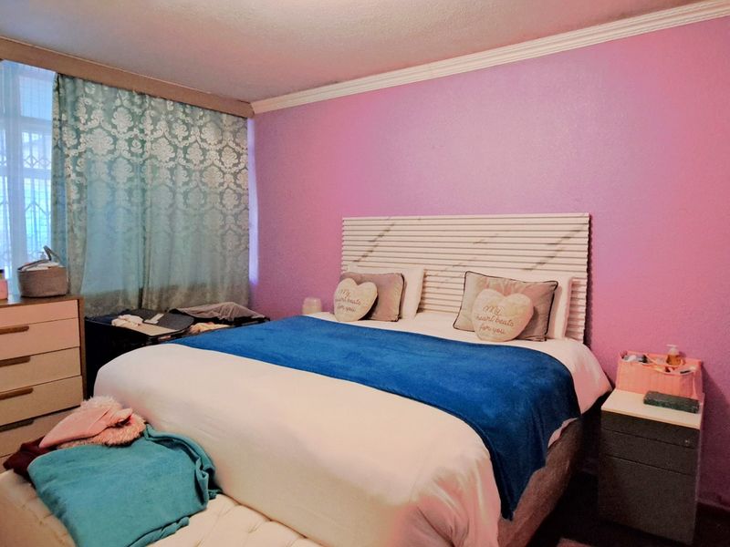 A bedroom featuring crown molding and security bars on the window, currently finished with a vibrant pink accent wall.