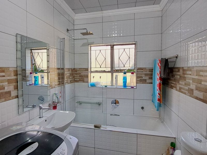 A functional bathroom featuring a combined bathtub and shower, basin, and toilet with neutral wall tiling and a tiled ceiling.