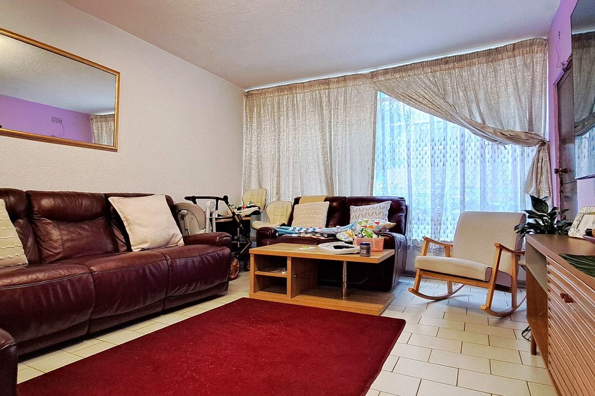 A comfortable living room featuring tiled flooring and a large window, providing a functional and well-lit space for relaxation.