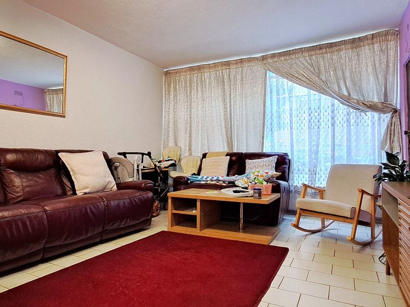 A comfortable living room featuring tiled flooring and a large window, providing a functional and well-lit space for relaxation.