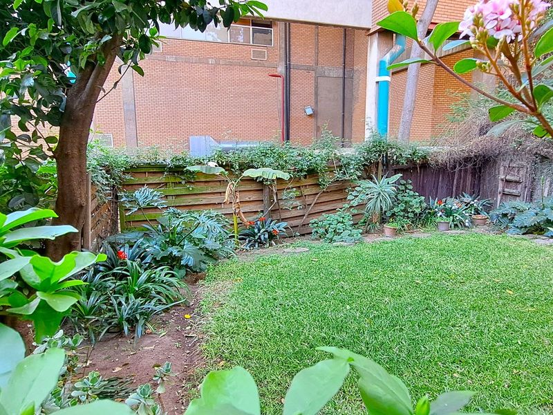A private garden area featuring a well-maintained lawn, mature trees, and wooden perimeter fencing.