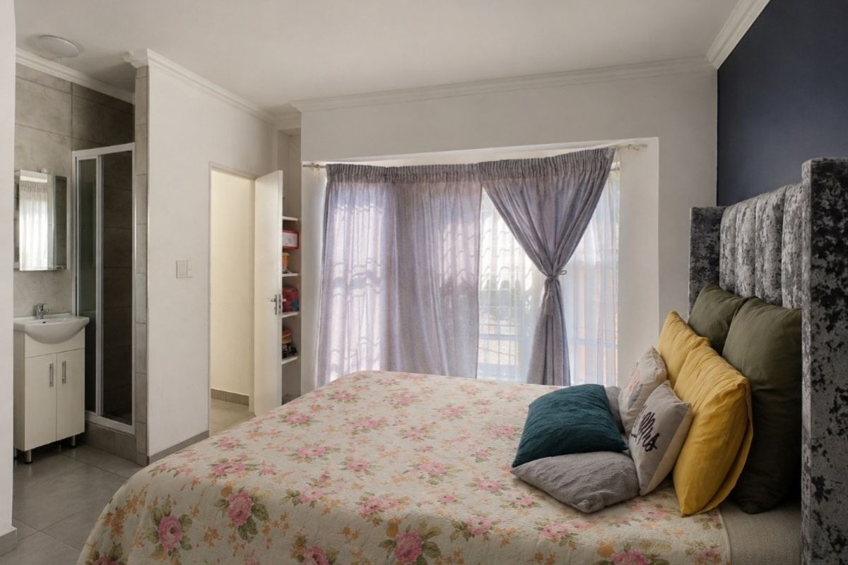 A well-maintained bedroom featuring an en-suite bathroom with a shower, built-in vanity, and integrated shelving, complemented by crown molding and tiled flooring.
