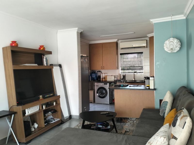 Open-plan living area featuring a compact kitchen with built-in cabinetry, integrated laundry space, and tiled flooring, creating a functional combined living and cooking environment.