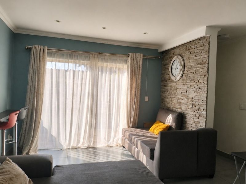 A bright living room featuring a textured stone cladding accent wall, tiled flooring, and large sliding glass doors providing natural light.