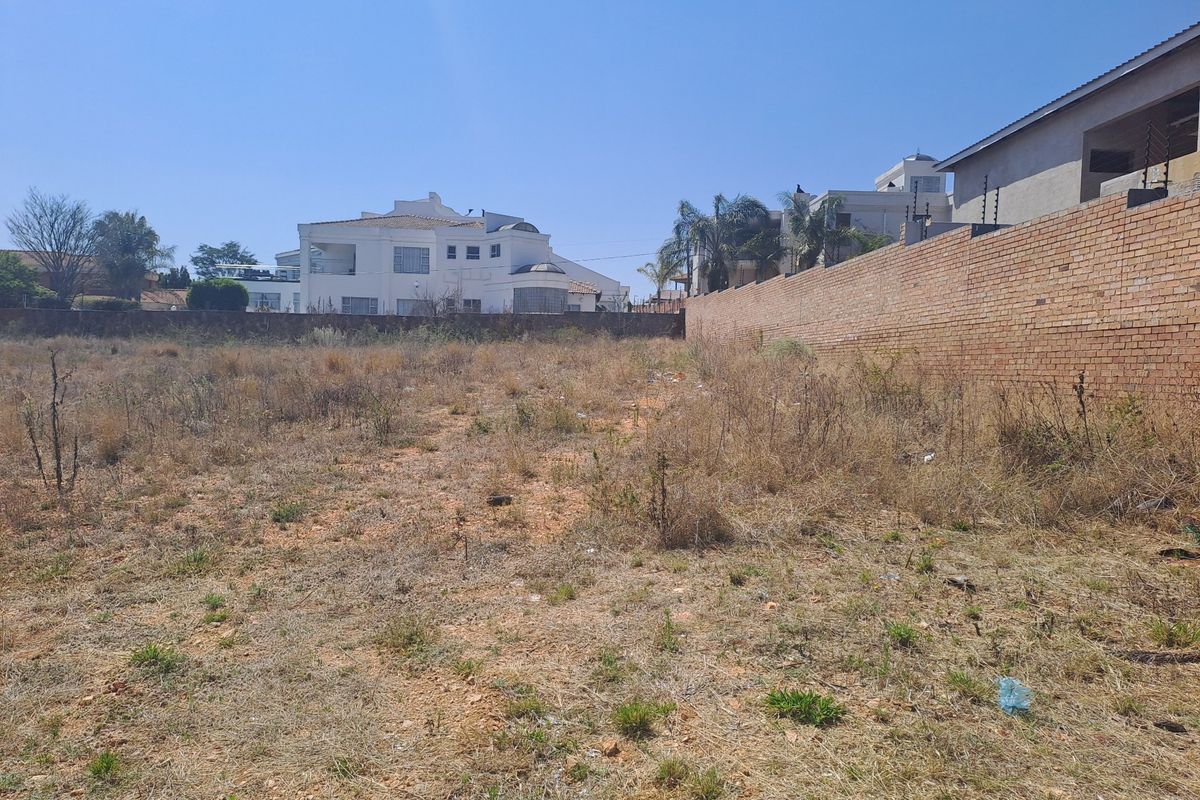 A vacant residential plot featuring a brick boundary wall with electric fencing, situated in an established neighborhood.