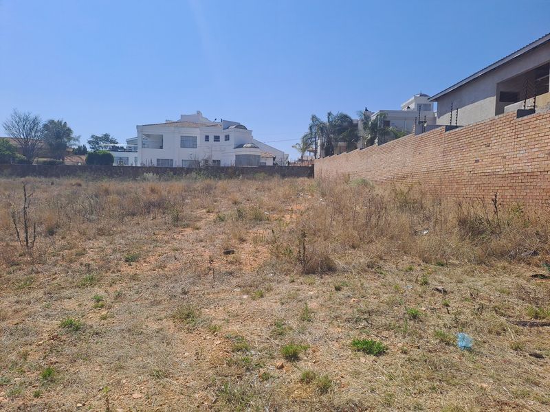 A vacant residential plot featuring a brick boundary wall with electric fencing, situated in an established neighborhood.