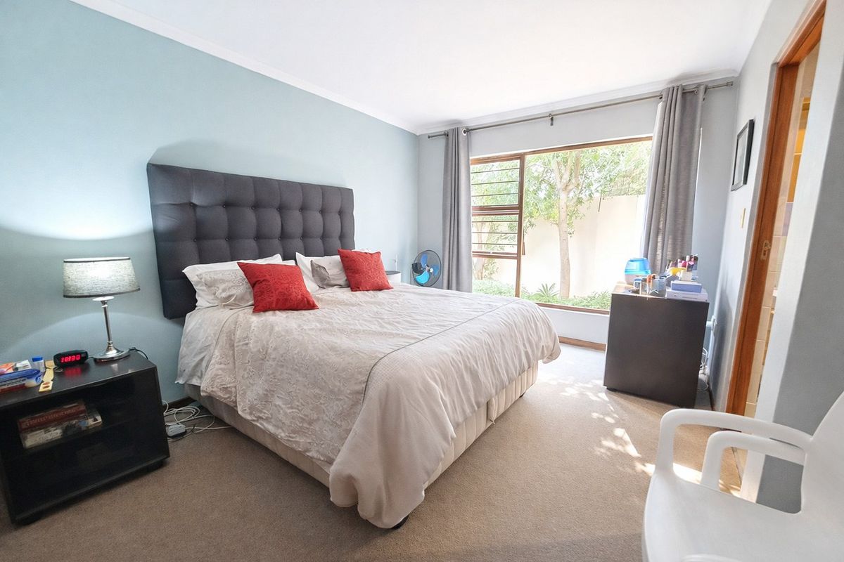 A well-lit bedroom featuring carpeted flooring, a large window with garden views, and neutral wall finishes.