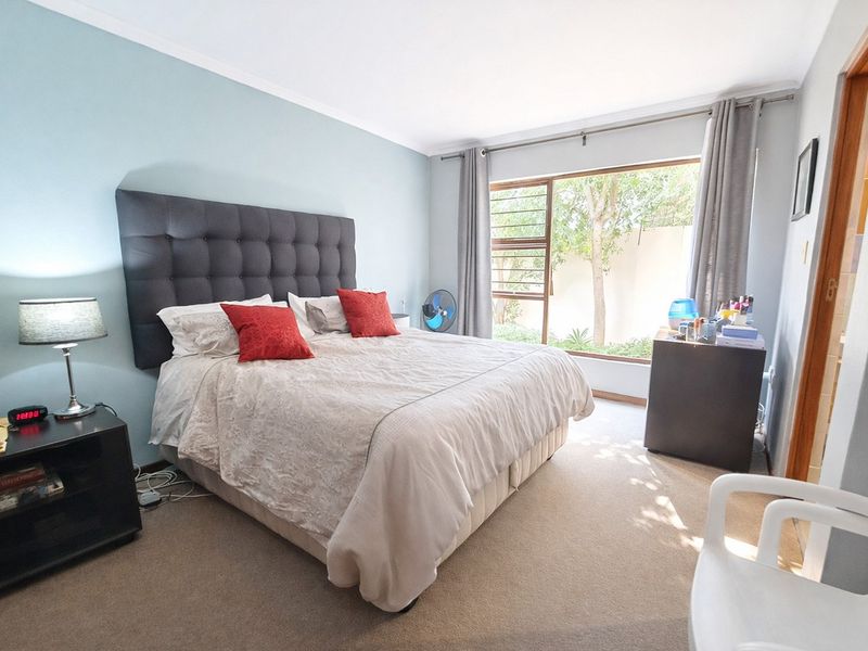 A well-lit bedroom featuring carpeted flooring, a large window with garden views, and neutral wall finishes.