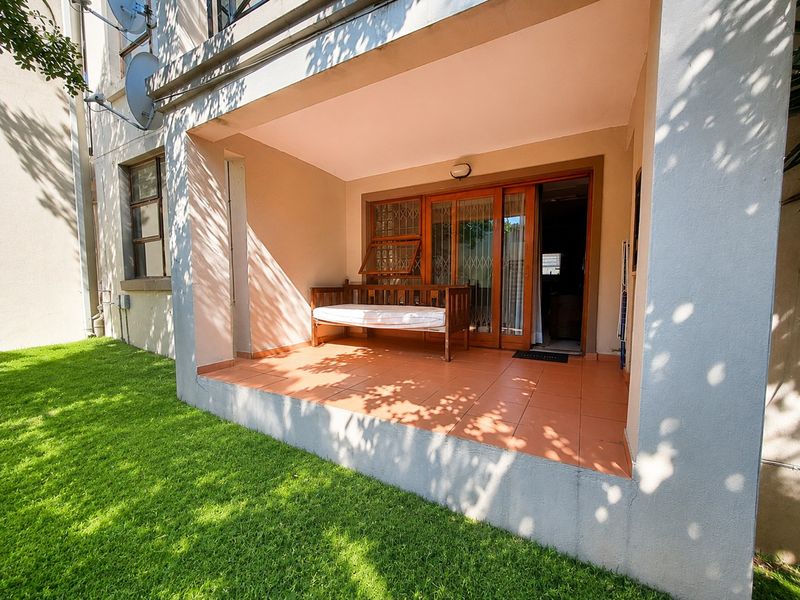 A covered patio area featuring tiled flooring and a sliding glass door with security gate, providing direct access to the garden.