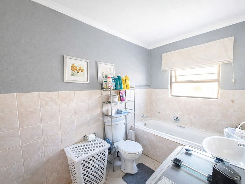 A functional bathroom featuring a bathtub, toilet, and washbasin with neutral wall tiling and grey painted upper walls.