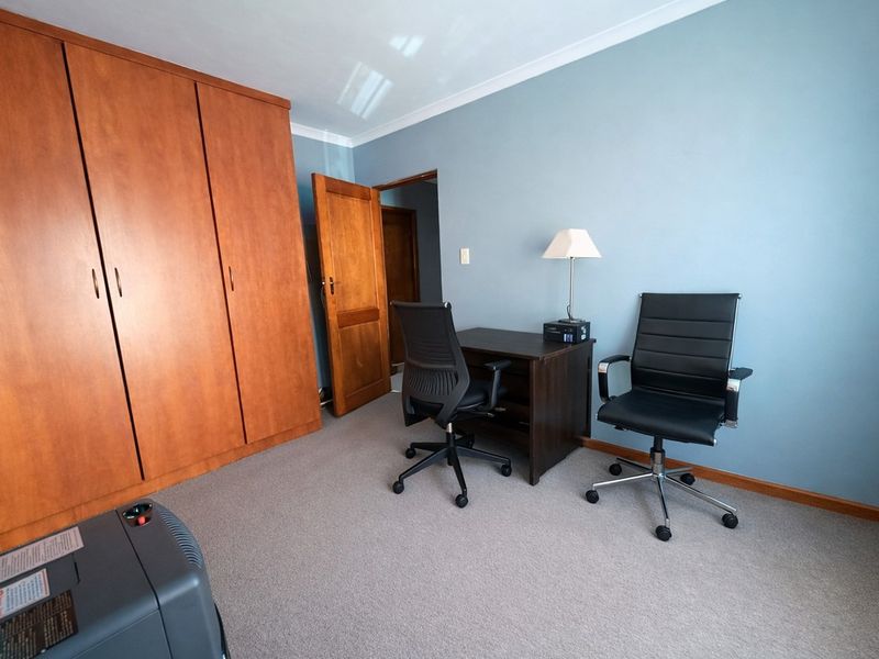 A bedroom featuring a large built-in wooden wardrobe, neutral carpeting, and blue painted walls with coving and skirting board details.