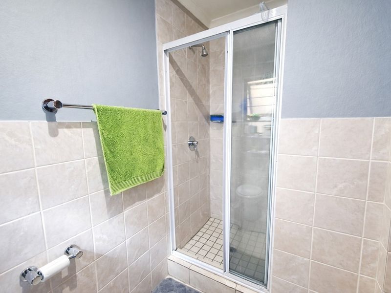 A functional bathroom featuring a tiled shower enclosure with a sliding glass door and neutral wall tiling.