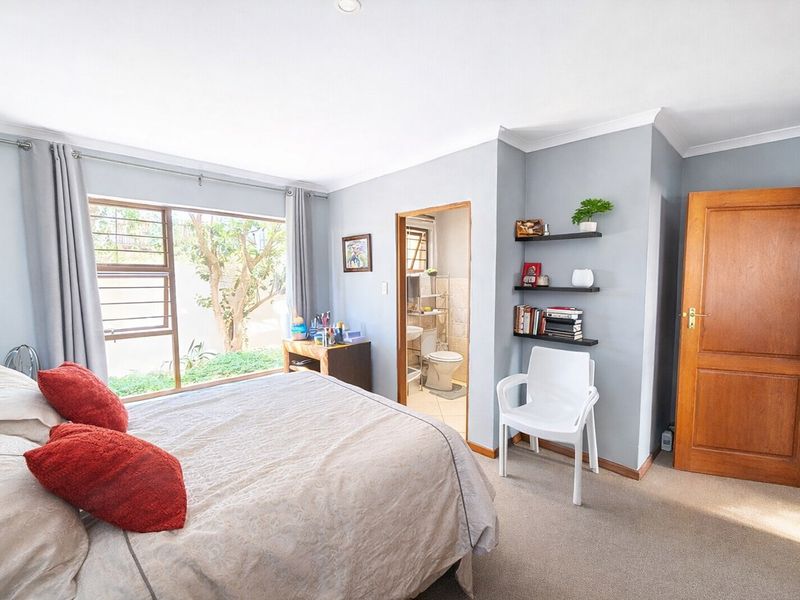 A bedroom featuring carpeted flooring, a large window with natural light, and an adjoining en-suite bathroom with a wooden door.