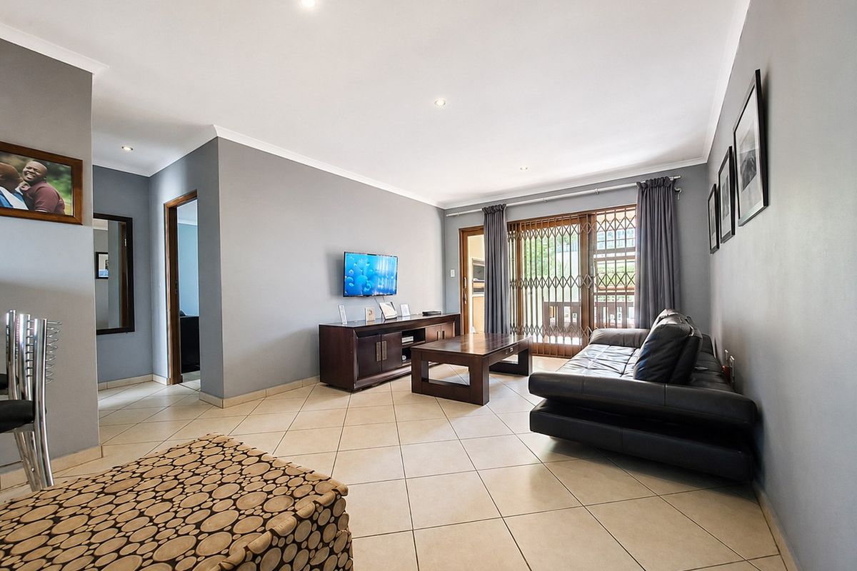 A spacious living room featuring neutral grey walls, tiled flooring, recessed downlights, and a sliding glass door leading to an outdoor area.