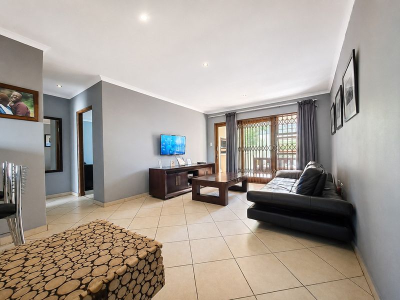 A spacious living room featuring neutral grey walls, tiled flooring, recessed downlights, and a sliding glass door leading to an outdoor area.