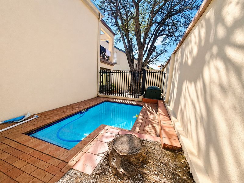 A private outdoor swimming pool area featuring brick paving, perimeter fencing, and a small garden space with a tree stump.