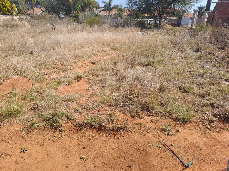 A view of a vacant residential plot featuring dry, overgrown grass and exposed soil, ready for development.