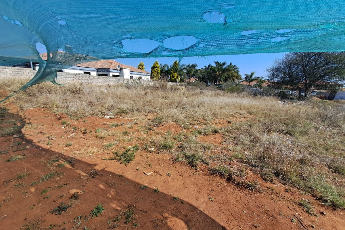 A vacant residential plot featuring natural ground cover and perimeter boundary walls, viewed through a damaged shade cloth screen.