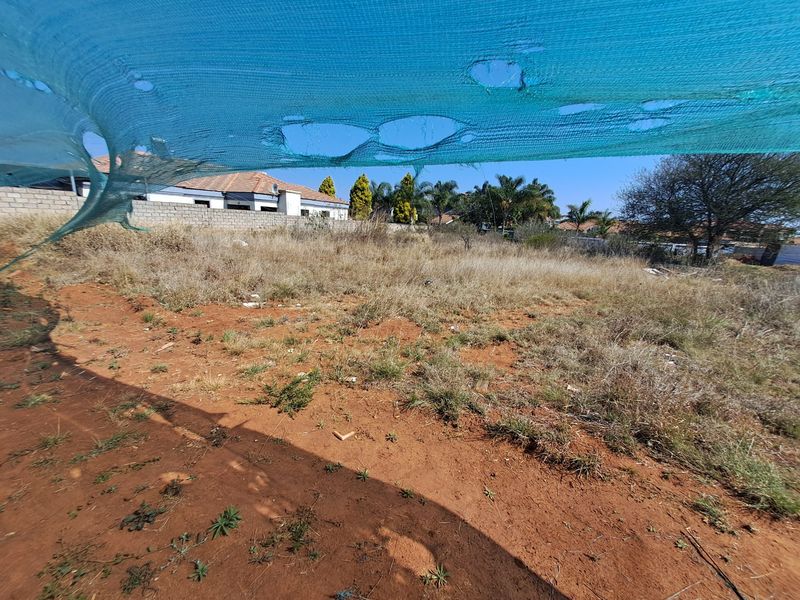 A vacant residential plot featuring natural ground cover and perimeter boundary walls, viewed through a damaged shade cloth screen.